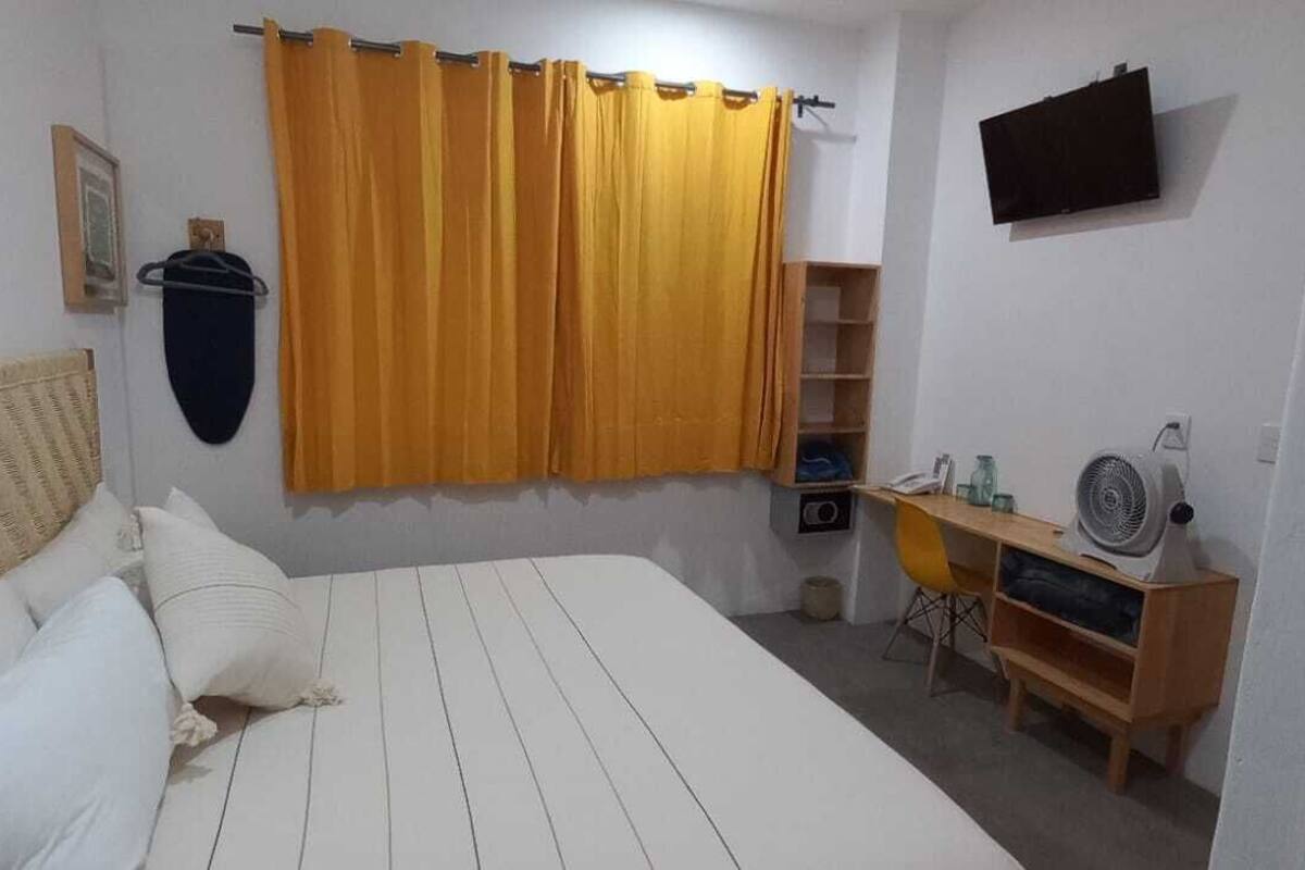 A bedroom with a bed, a TV, a fan, and a shelf with items.