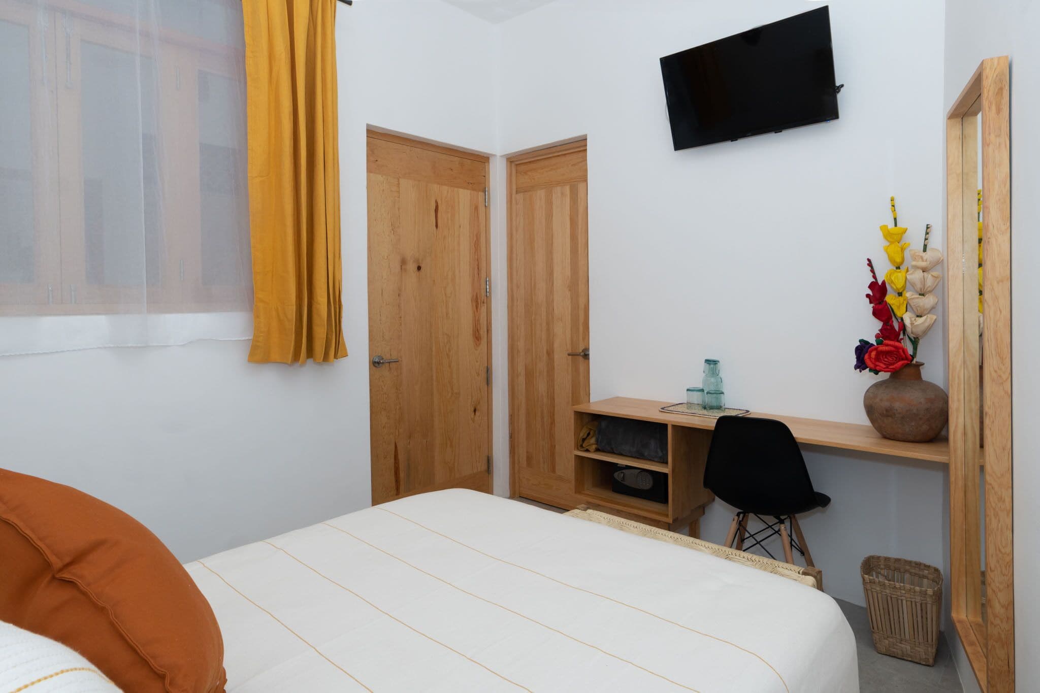 A bedroom with a bed, a desk, a chair, a TV, and a mirror.