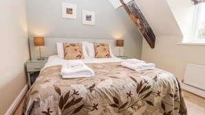 A bedroom with a sloped ceiling, a bed with floral bedding, two bedside lamps, and two framed pictures on the wall.