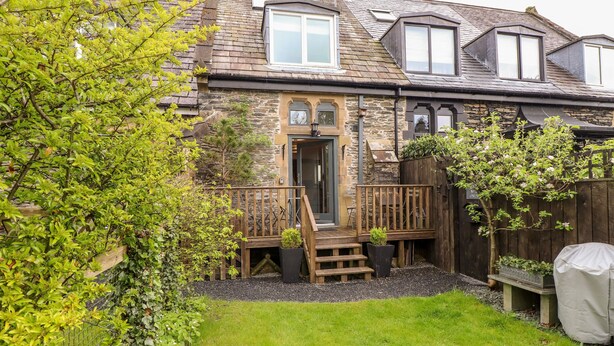A stone house with a wooden deck, a front door, and a small garden area.