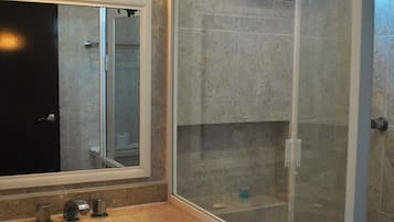 Een badkamer met een marmeren wastafel, een grote spiegel en een douche met glazen wanden.