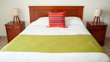 Een netjes opgemaakt bed met een groene deken, een gestreept kussen en twee nachtkastjes met lampen.