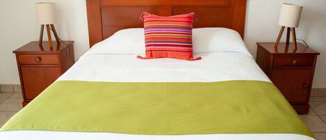 A neatly made bed with a green throw blanket, a striped pillow, and two bedside tables with lamps.