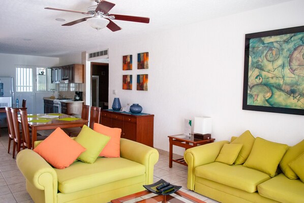 A living room with two yellow sofas, a ceiling fan, and a painting on the wall. - Tan Ik Beachfront Condos (Akumal)