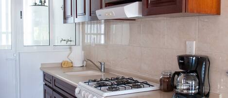 A kitchen with wooden cabinets, a gas stove, an oven, a coffee maker, and a trash bin.