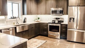 Et moderne køkken med rustfrie stålgre, mørke træskabe og et backsplash med fiskebensmønstret fliser.