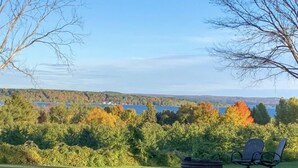 A grassy area with a bench and a small table, overlooking a lake and trees with autumn foliage.
