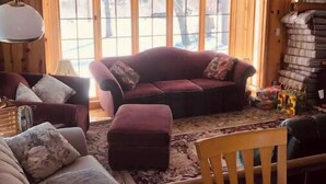 A cozy log cabin interior with a large window, wooden furniture, and a fireplace.