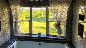 A bathroom with a large window, a bathtub, and a view of a green landscape.