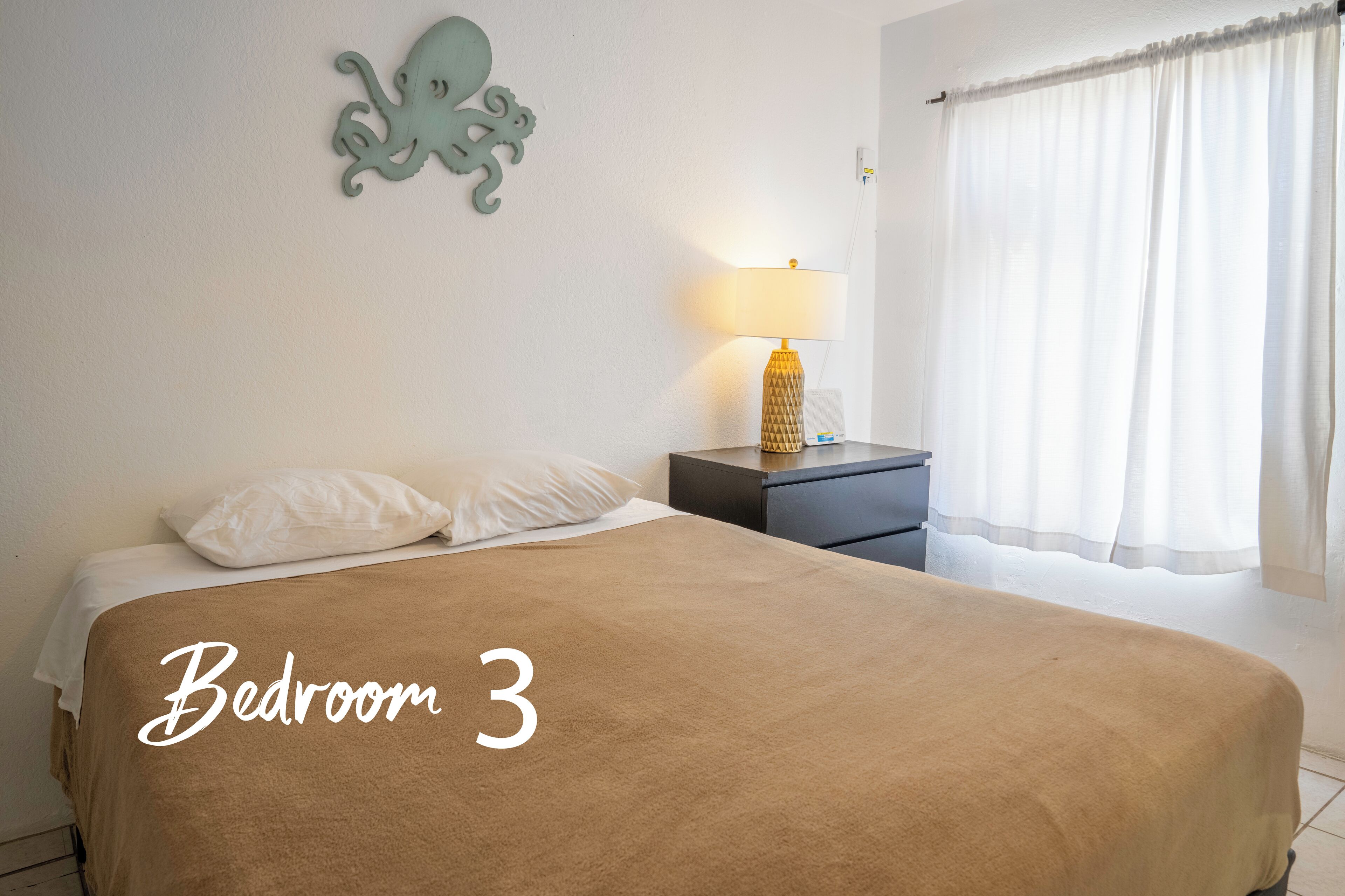 A bedroom with a large bed, a nightstand with a lamp, and a wall decoration.