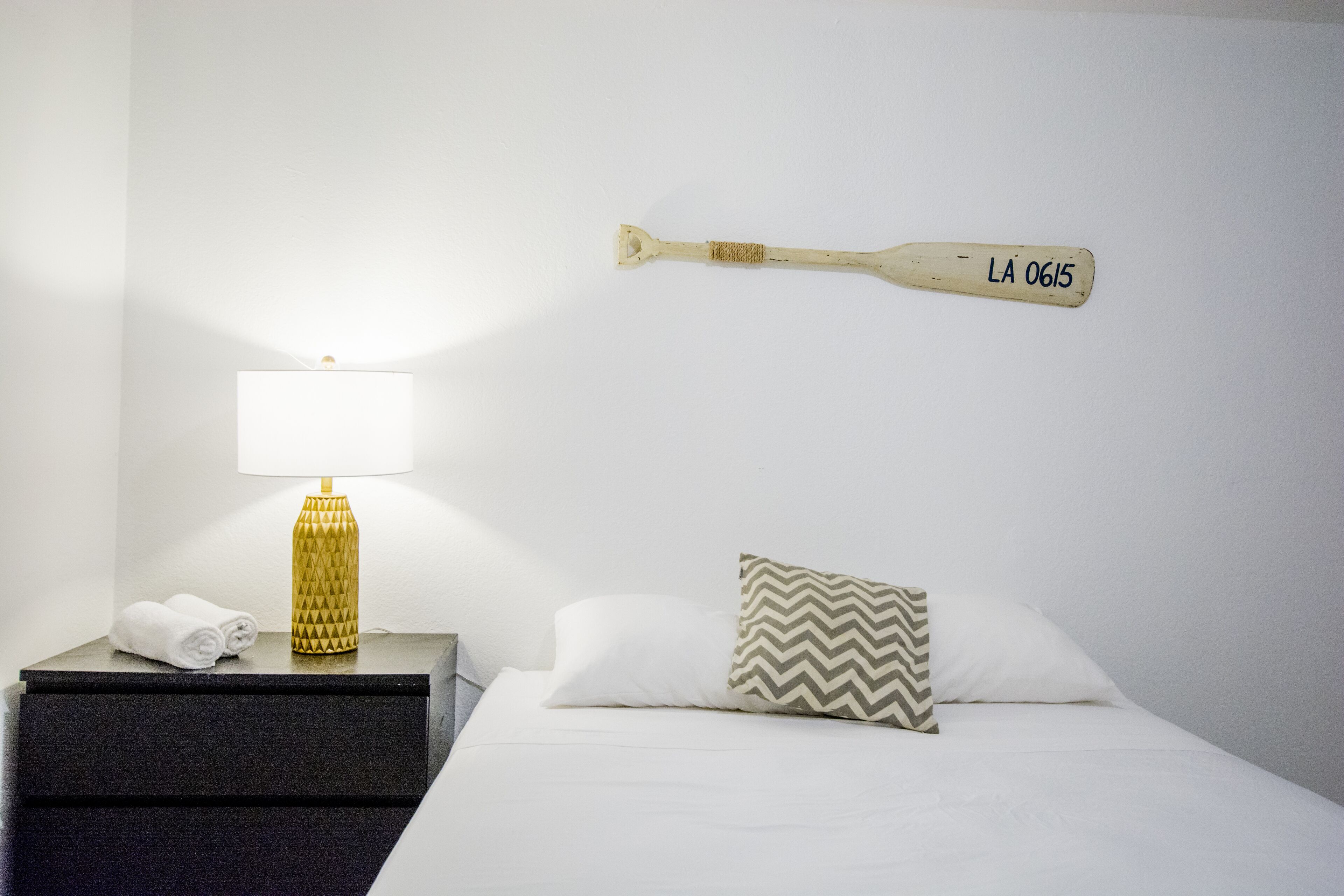 A neatly made bed with a pillow, a bedside lamp, and a towel on a nightstand.