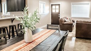 Een eethoek met een donker houten tafel, stoelen, een potplant en een gestreept tapijt.