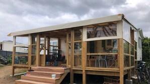 Estructura de madera con porche cubierto y varias ventanas, con mobiliario exterior y bicicletas.