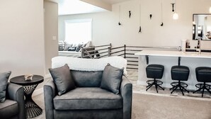 Ein modernes Wohnzimmer mit grauem Sofa, einem kleinen runden Tisch und einer Bar mit Hockern.