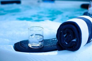 Ein Glas Wasser mit Eiswürfeln auf einer schwarzen Matte neben einem zusammengerollten Handtuch am Pool.