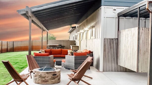 Eine Außenpatio-Terrasse mit überdachter Sitzgruppe, einem Feuerkorb und Blick auf den Garten.