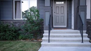 A house with a gray front door, a stone accent wall, and a small front yard with a lawn and shrubs.
