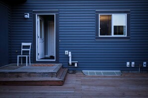 Una casa con terraza de madera, una puerta blanca y una ventana con persianas.