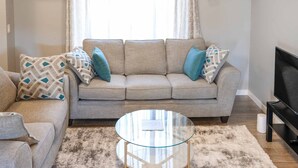 A living room with a beige sofa, a glass coffee table, and a television on a stand.