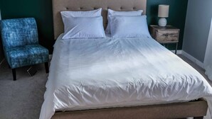 A neatly made bed with white linens, a tufted headboard, and a wooden nightstand with a lamp.