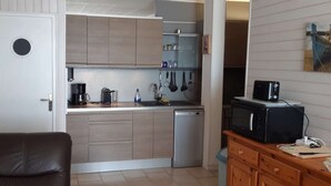 Una cucina compatta con lavastoviglie, macchina da caffè e forno a microonde. Si nota un pensile in legno e un piccolo piano di lavoro.