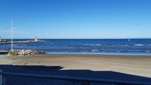Una spiaggia con un litorale roccioso, un faro e una barca all'orizzonte.