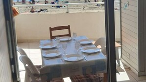 Zona pranzo con tavolo apparecchiato per quattro, vista su una spiaggia con persone e ombrelloni.