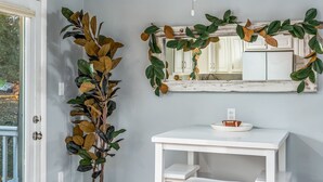 Una stanza con una toeletta bianca, uno specchio decorato con una ghirlanda di foglie e una pianta in vaso.