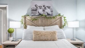 Camera da letto con un letto, due comodini, una lampada, un cuscino soffice e un quadro appeso al muro.