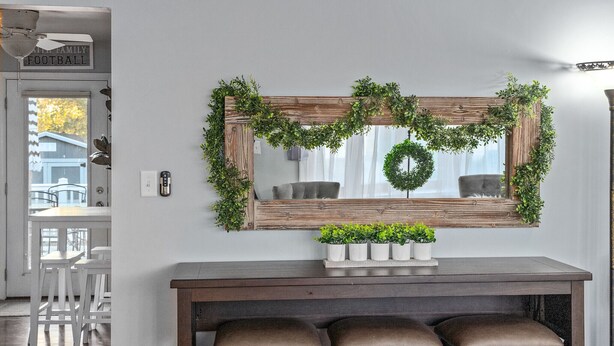 Un'area pranzo con tavolo in legno, tre sgabelli da bar e uno specchio decorato con una ghirlanda verde.
