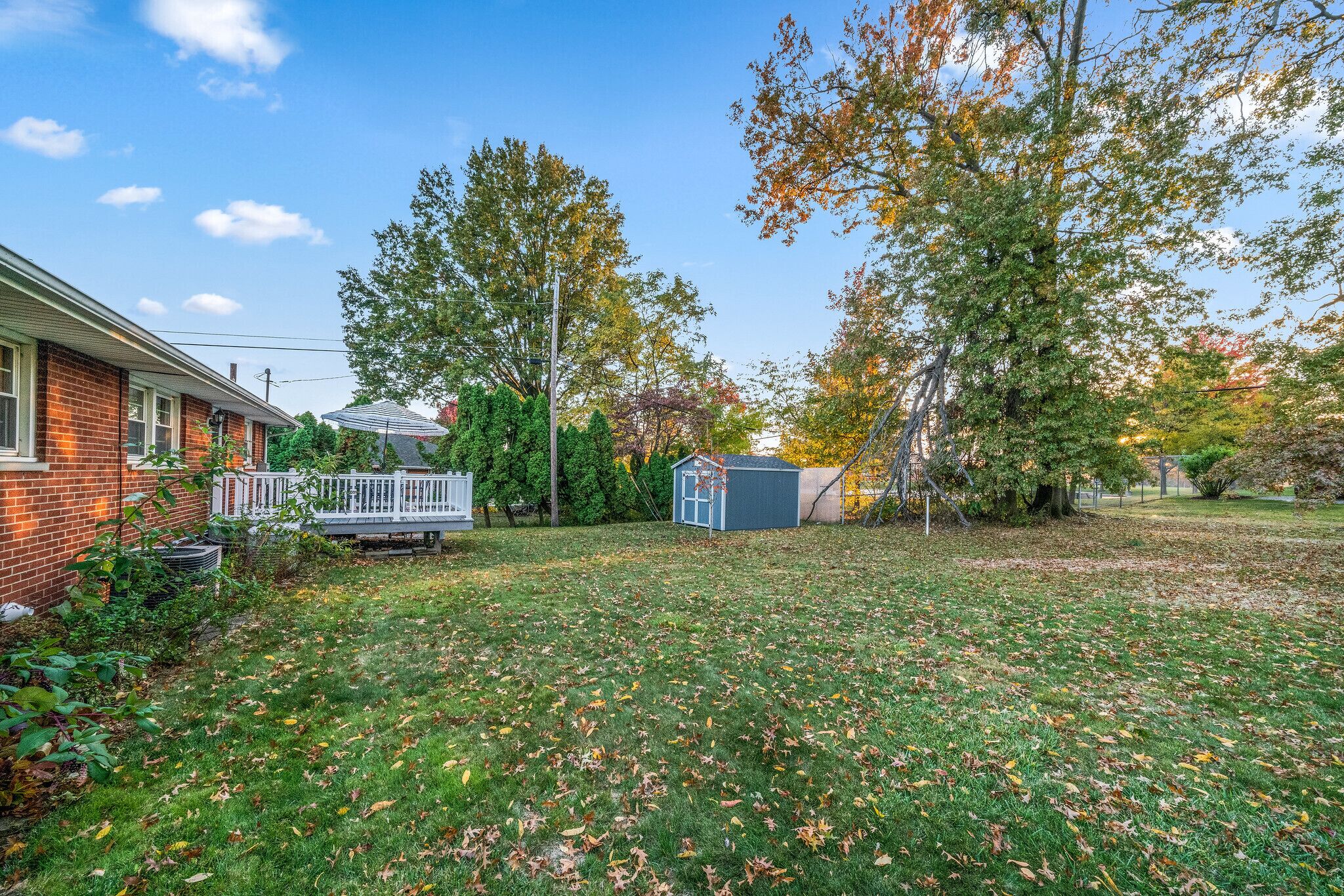 A residential backyard with a brick house, a wooden deck, and a shed.