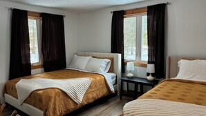 Ein Hotelzimmer mit zwei Betten, einem kleinen Tisch mit Lampen und einem Fenster mit Vorhängen.