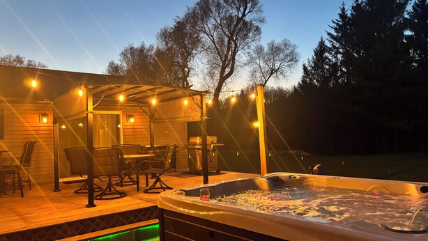 Eine Außenpatio mit Whirlpool, Lichterketten und einer überdachten Sitzgelegenheit.