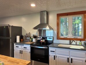 A modern kitchen with a stainless steel refrigerator, oven, and stove, a wooden countertop, and a window with a view of trees.