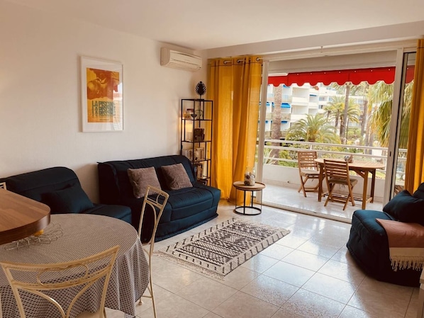 A living room with a sofa, a small round table, a bookshelf, and a balcony with a table and chairs.
