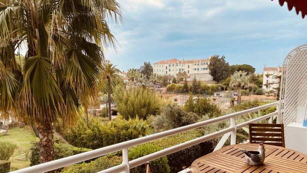 A balcony with a wooden table and chairs, overlooking a garden and buildings. - Large studio in Cannes-MON2 (CANNES)