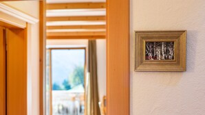 Un couloir avec des poutres en bois, un tableau encadré au mur et une porte donnant sur une pièce lumineuse.