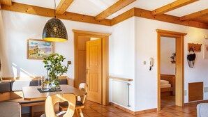 Un intérieur moderne avec une table à manger en bois, des chaises, un banc, un luminaire suspendu et une porte donnant sur une chambre.