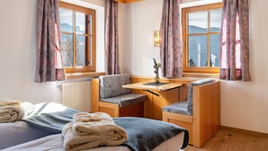 Une chambre avec un lit, deux chaises, une petite table et une vue sur les montagnes grâce à de grandes fenêtres.