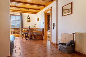 A cozy room with a wooden ceiling, a dining area with a table and chairs, a bench, and a view of mountains through a window.