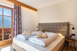 Un dormitorio con una cama grande, cabecera, mesita de noche, ventana con cortinas y vista a las montañas.
