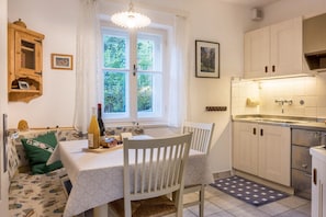 A kitchen with a dining area, a window with curtains, a wooden cabinet, and a tiled floor.
