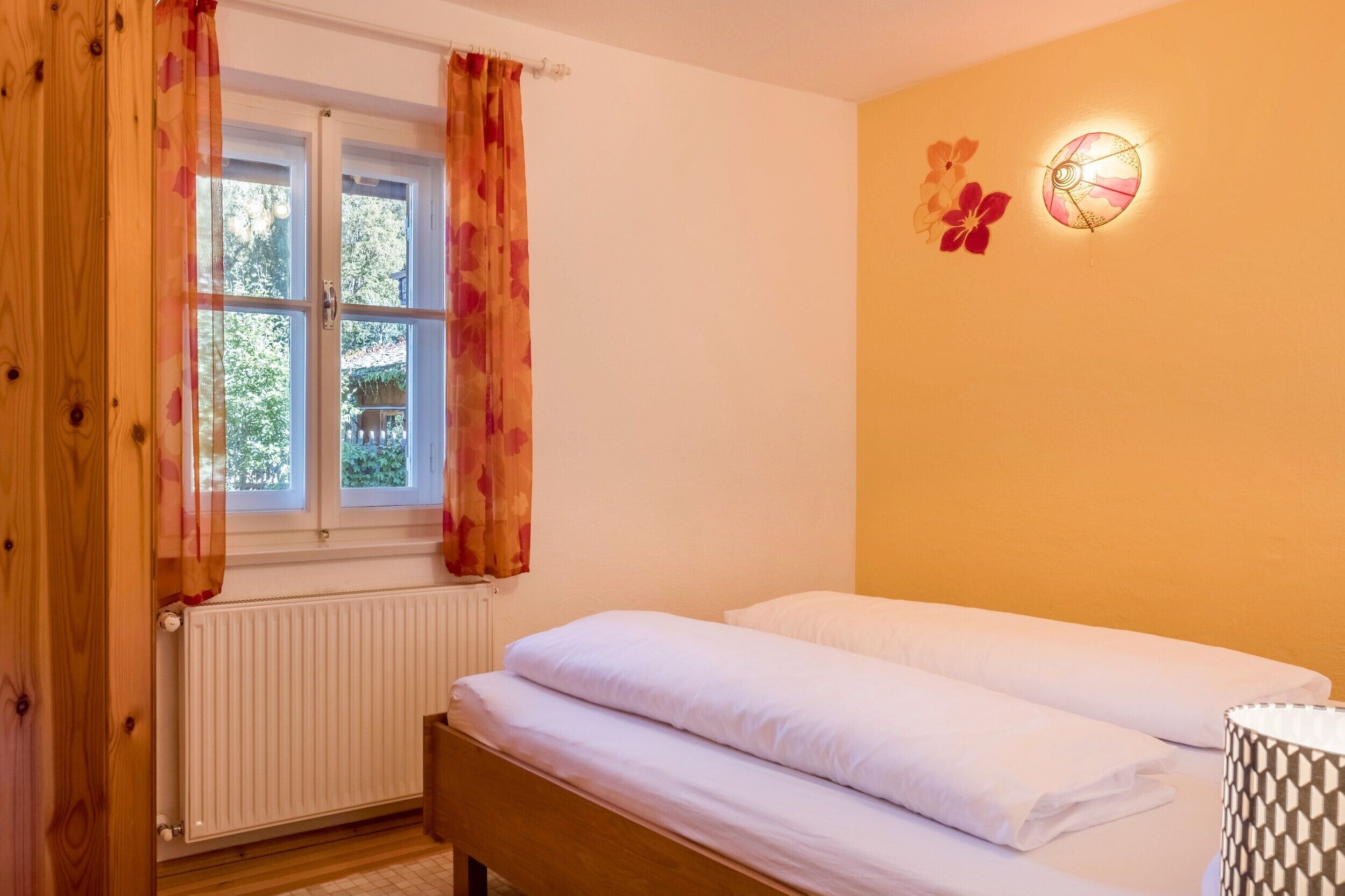 Una habitación con cama, radiador, ventana con cortinas e iluminación en la pared.