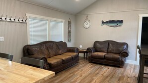 A spacious living room with two brown leather sofas, a wooden coffee table, and a dining table. - Cute cabin in nice quiet secluded area close to the water, The Coves Golf course (Afton)