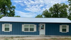 A single-story building with a metal roof, a front door, and two windows with shutters. - Cute cabin in nice quiet secluded area close to the water, The Coves Golf course (Afton)