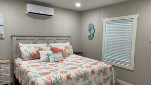 A bedroom with a bed, a nightstand, an air conditioner, a window with blinds, and a decorative seahorse on the wall. - Cute cabin in nice quiet secluded area close to the water, The Coves Golf course (Afton)