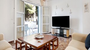 Een woonkamer met een houten tafel, twee beige banken, een flatscreen televisie en een schuifdeur naar een buitengebied.