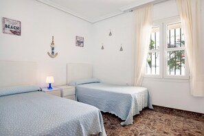 A bedroom with two beds, a nightstand, a lamp, and a window with curtains.