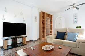 A living room with a flat-screen TV, a wooden bookshelf, a beige sofa, and a ceiling fan.