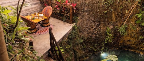 Un comedor con una mesa dispuesta para dos personas, rodeado de exuberante follaje y vista a una fuente de agua.